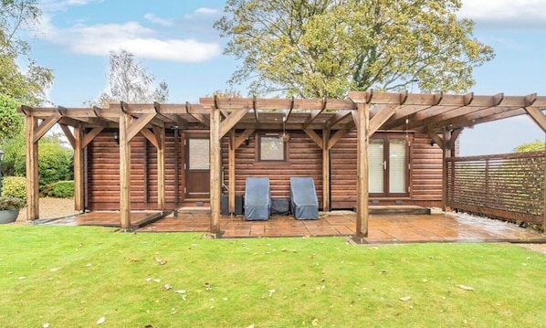 Una estructura de pérgola de madera con un patio, dos sillas y una valla de madera.