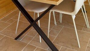 Ein Esszimmer mit einem Holztisch, vier Stühlen, schwarzem Metallgestell und Fliesenboden.