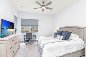 Een slaapkamer met een bed, bureau, stoel, televisie en plafondventilator.