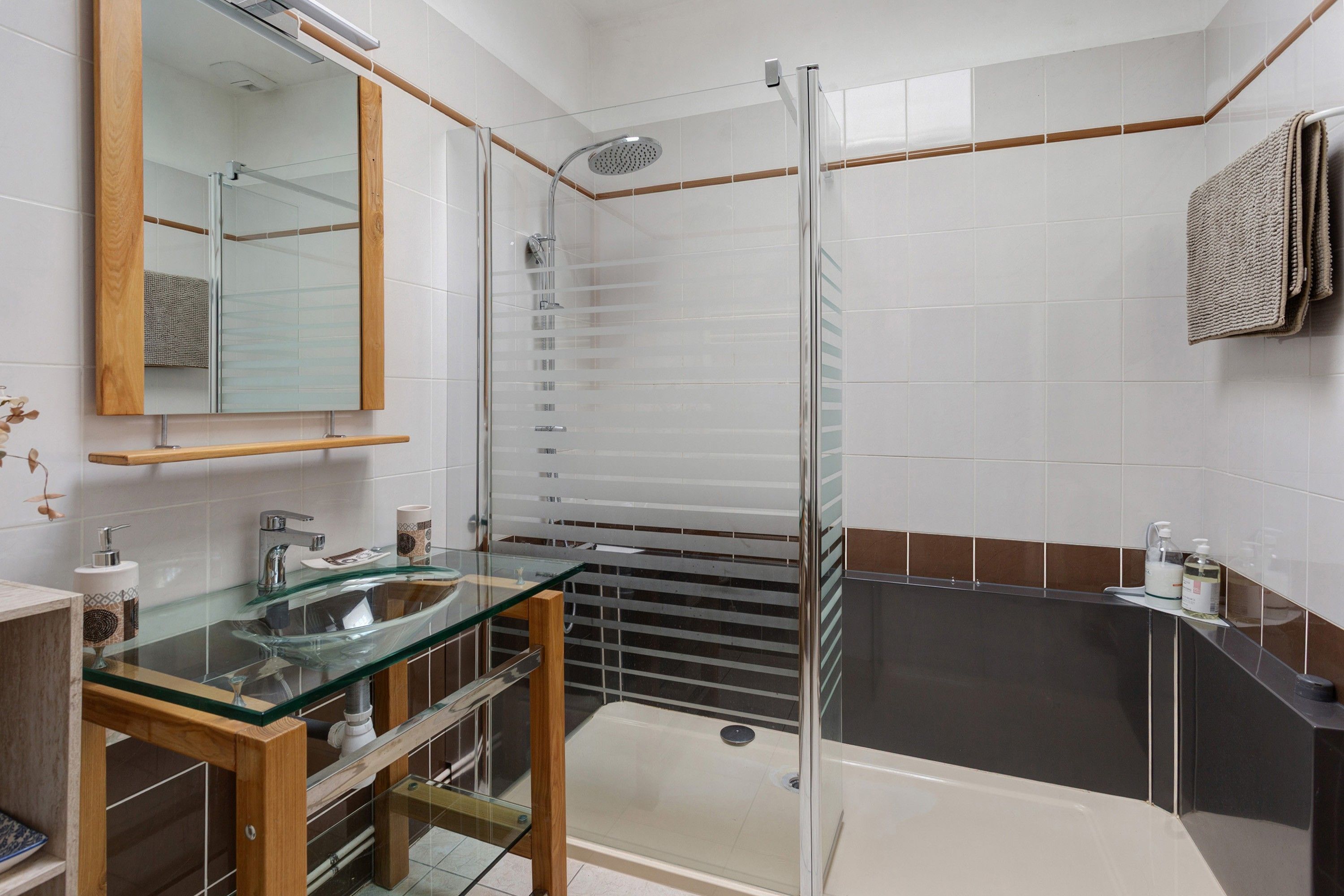 A modern bathroom with a glass shower enclosure, a glass sink, and a separate bathtub area.