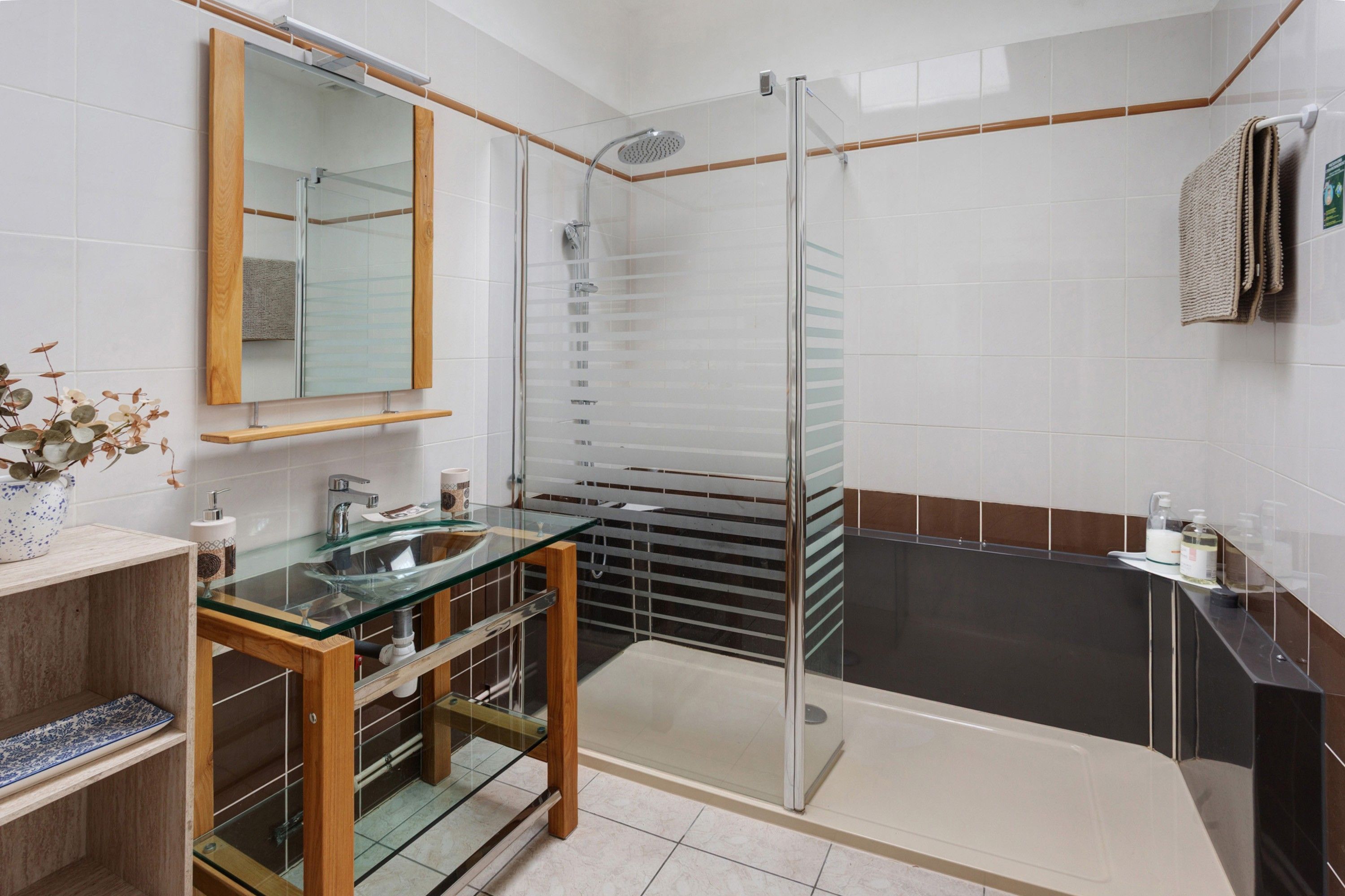 Een moderne badkamer met een douchecabine van glas, een glazen wastafel en een houten wastafelmeubel.