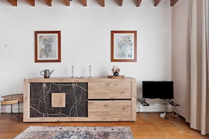 A room with a wooden cabinet, two framed artworks on the wall, a television, and a patterned rug.
