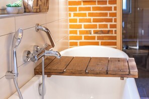 A bathroom with a white bathtub, a wooden shelf, and a brick wall. - Vrbo Property (Bleckede)