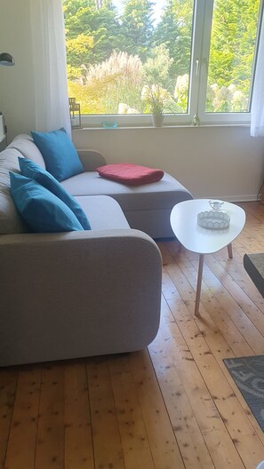 A modern living room with a grey sofa, blue cushions, a red throw, and a white coffee table.