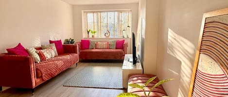Una sala moderna con un sofá rojo, una segunda zona de estar y un gran ventanal con persianas.