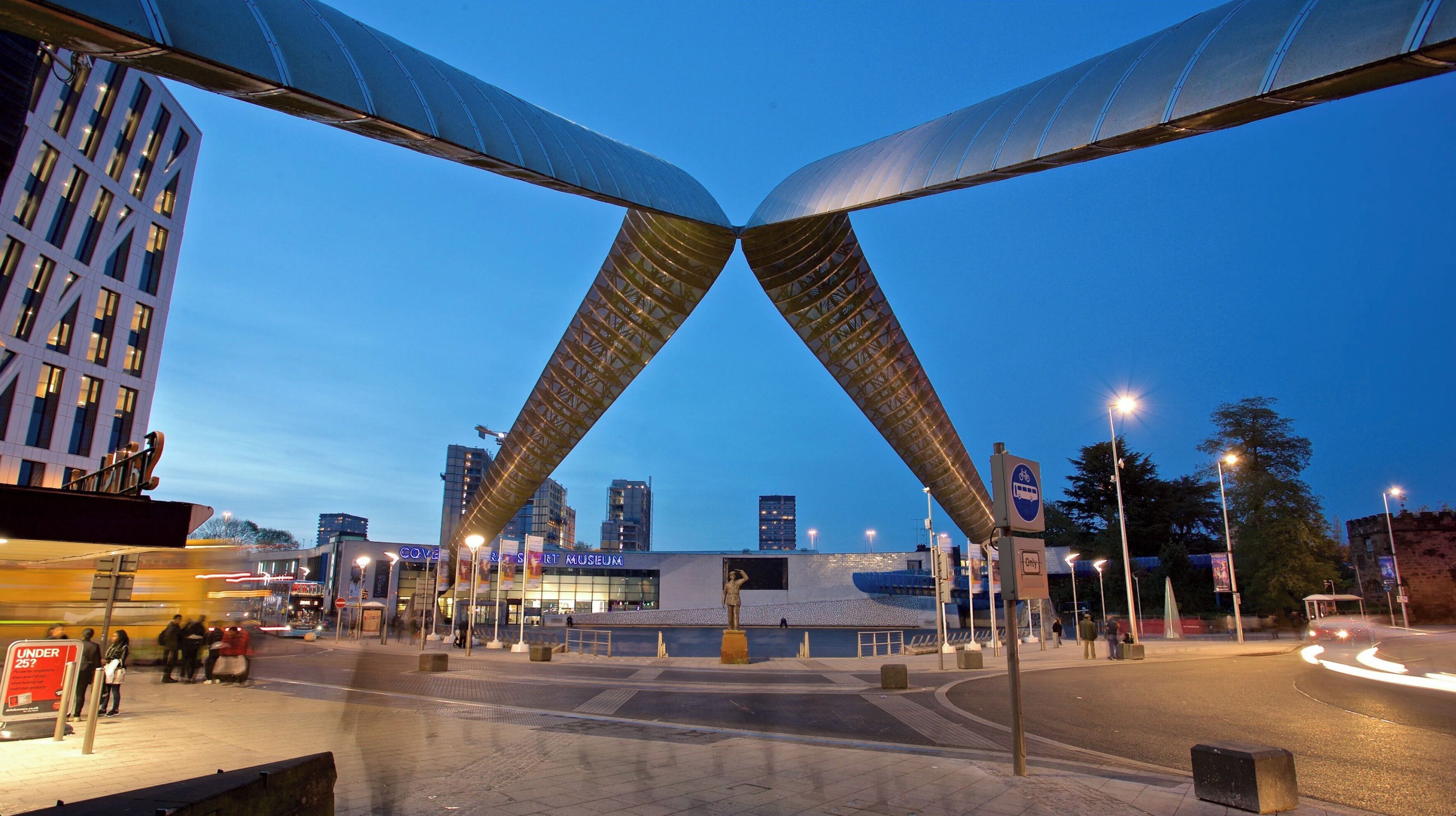 Een modern stadsplein met een opvallende brugconstructie, een museum en een gebouw met de naam 'COVE'.