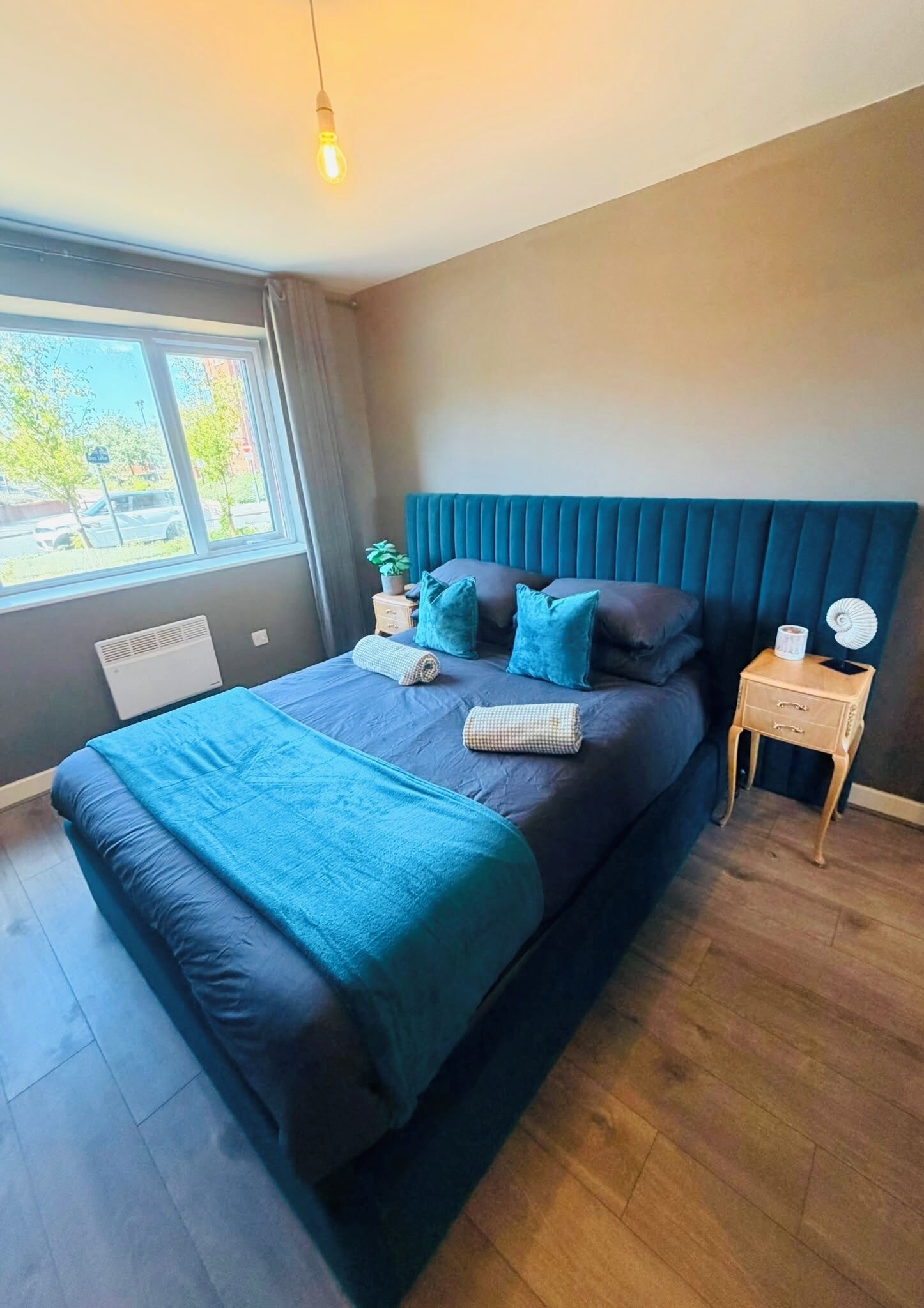 A modern bedroom with a large bed, a bedside table, a nightstand, and a window with curtains.