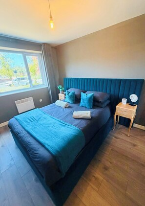 A modern bedroom with a large bed, a bedside table, a nightstand, and a window with curtains. - Hearth Residences - A perfect Home for Your Stay (Coventry)