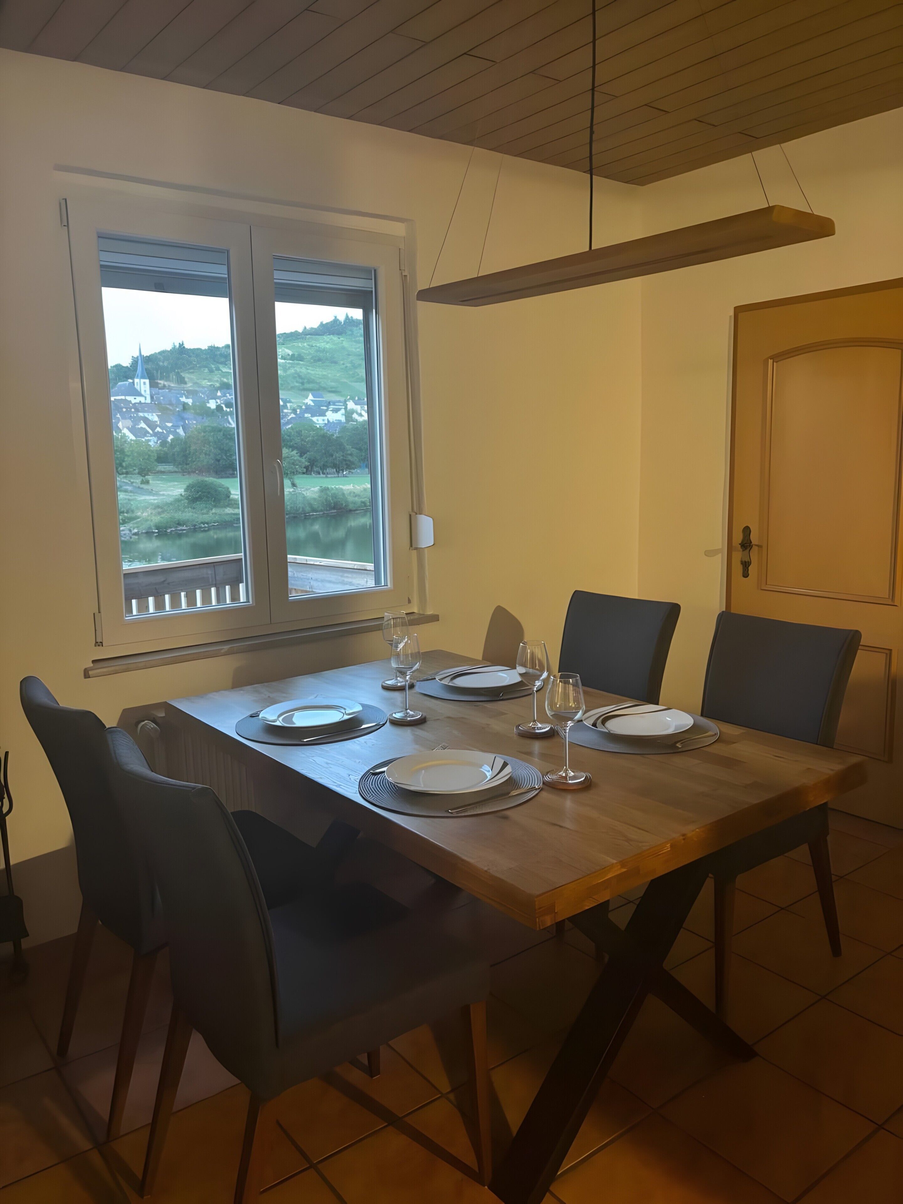A dining area with a wooden table set for four, chairs, and a view of a landscape through a window.