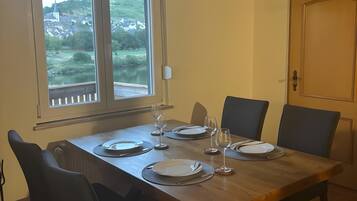 A dining area with a wooden table set for four, chairs, and a view of a landscape through a window.