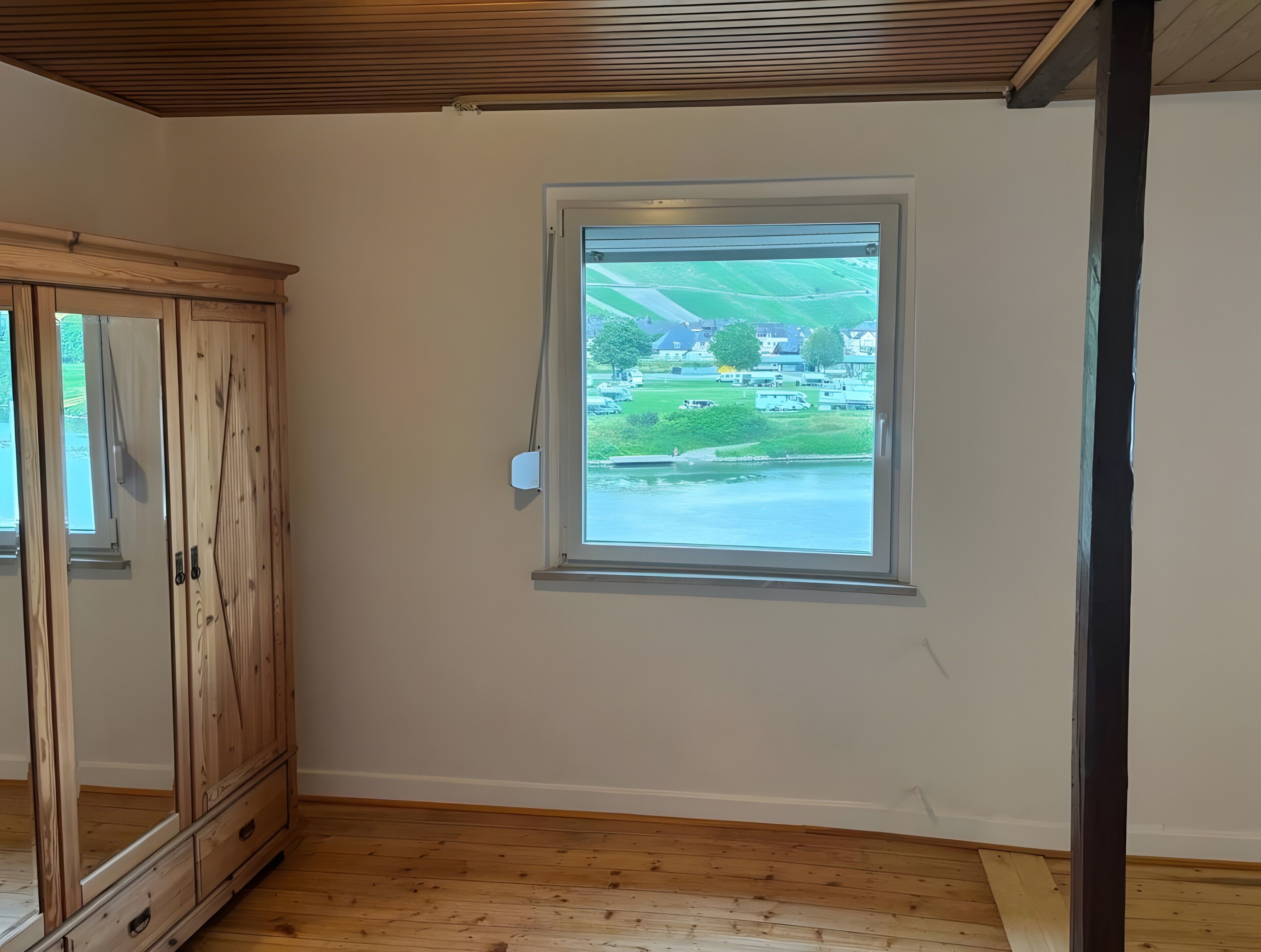 Une pièce avec un meuble en bois, une fenêtre donnant sur un paysage verdoyant et un plancher en bois.