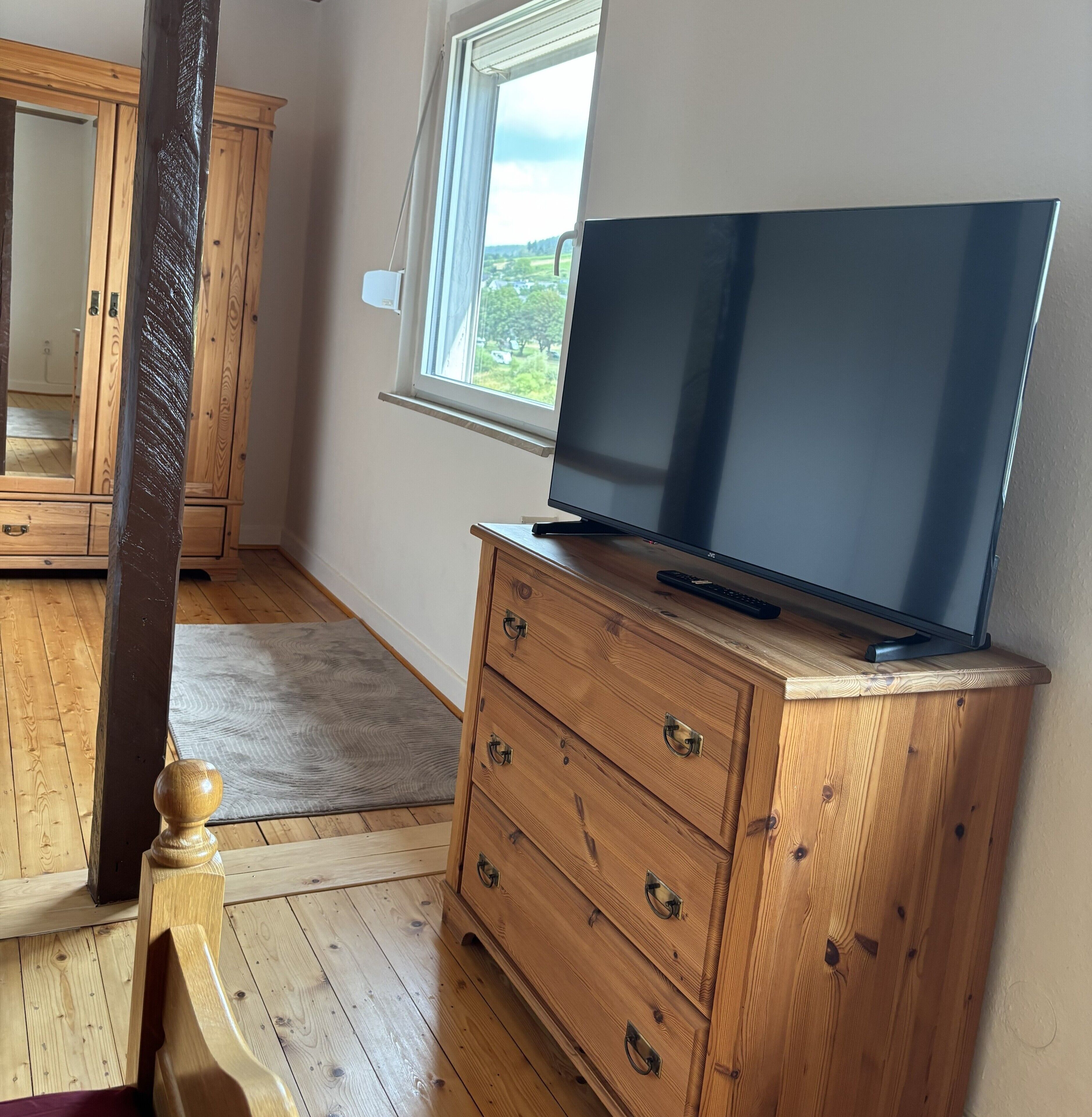 Ein Zimmer mit einem Holzkasten, einem Flachbildfernseher und einem Fenster mit Blick auf Grünflächen.