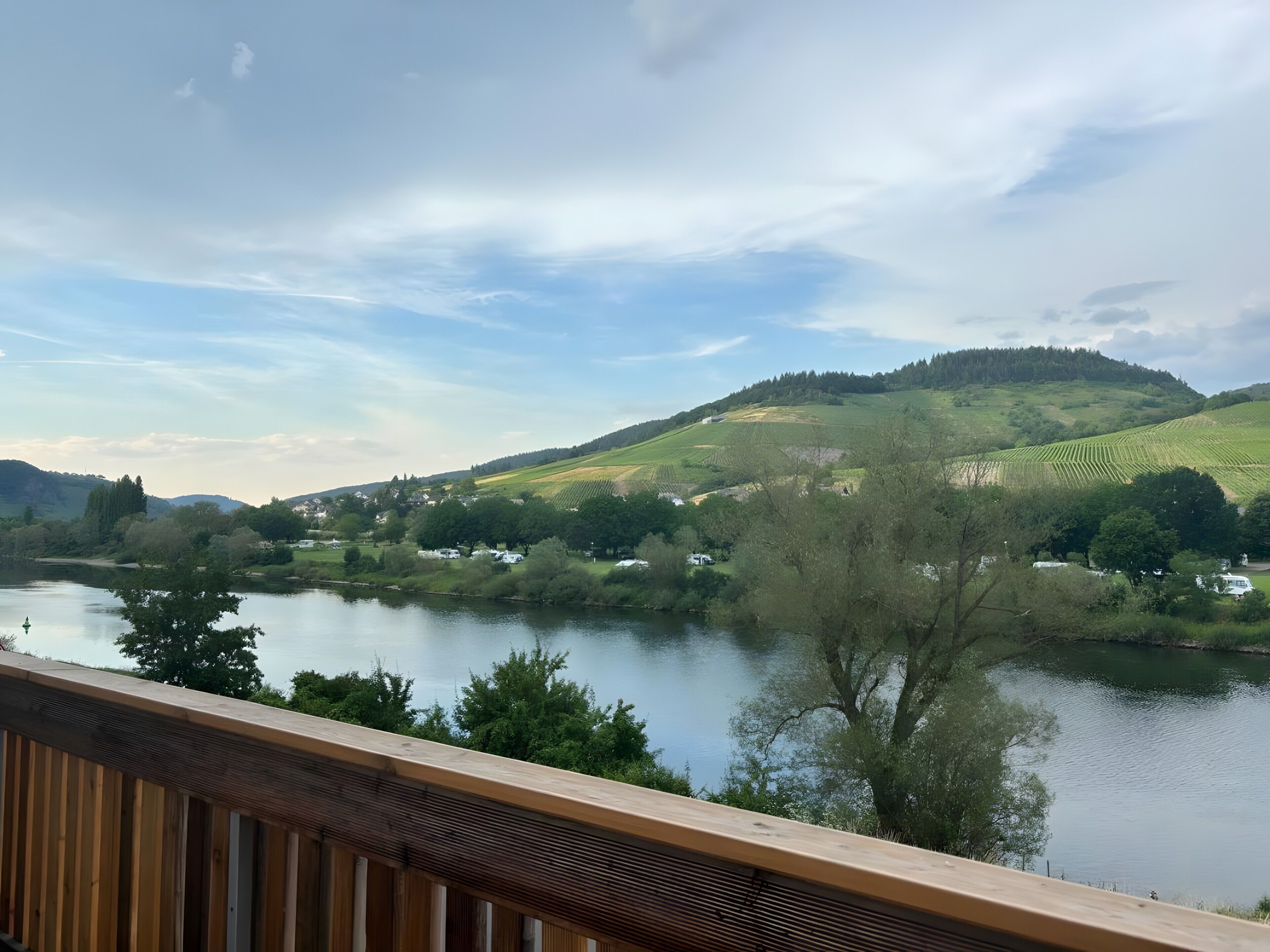 Ein Fluss mit einem hölzernen Deck, das auf ein Tal mit Häusern und viel Grün blickt.