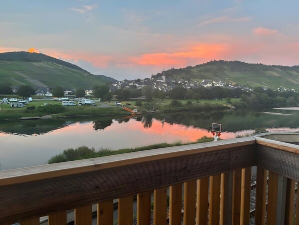 Vista de un lago con una terraza de madera, un aro de baloncesto y un pueblo al fondo.