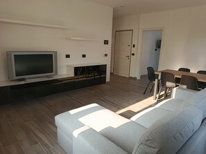 Un saló modern amb televisió de pantalla plana, un sofà gris, una taula de dinar amb cadirees i una llar de foc.