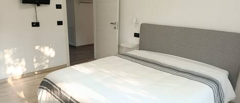 A bedroom with a bed, a television mounted on the wall, and a door leading to another room.