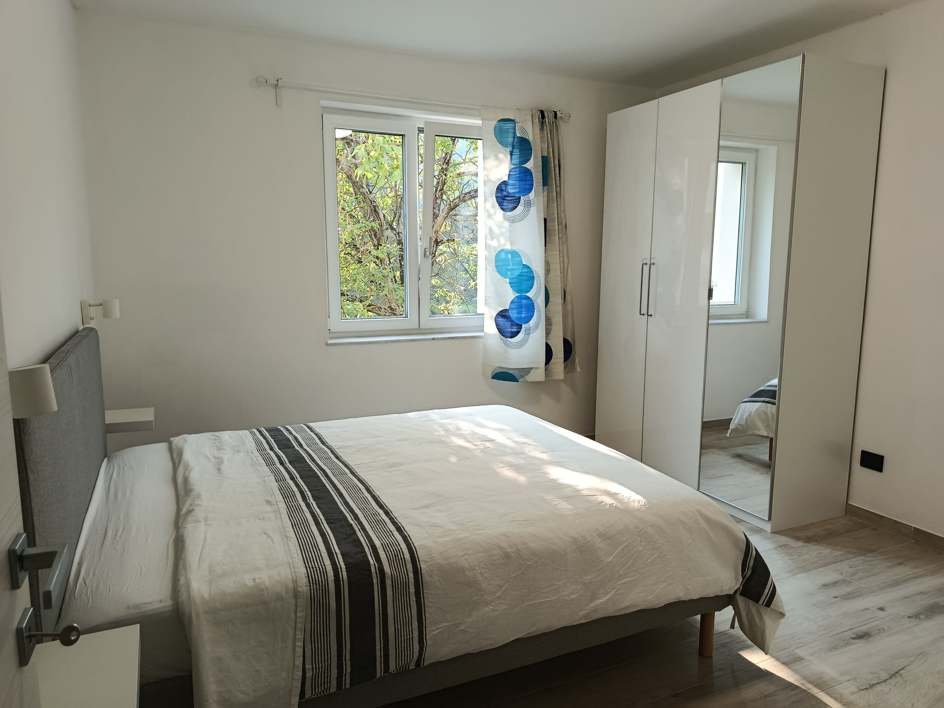A bedroom with a bed, a window with curtains, a wardrobe, and a mirror.