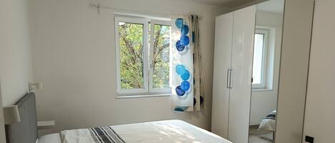 A bedroom with a bed, a window with curtains, a wardrobe, and a mirror.