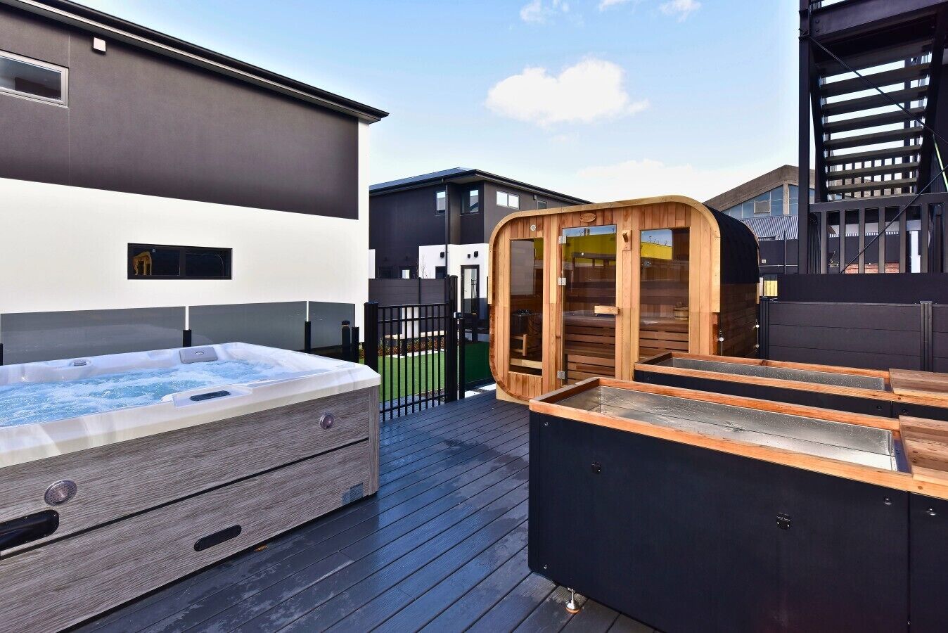 A hot tub and sauna on a wooden deck, with a modern building in the background.