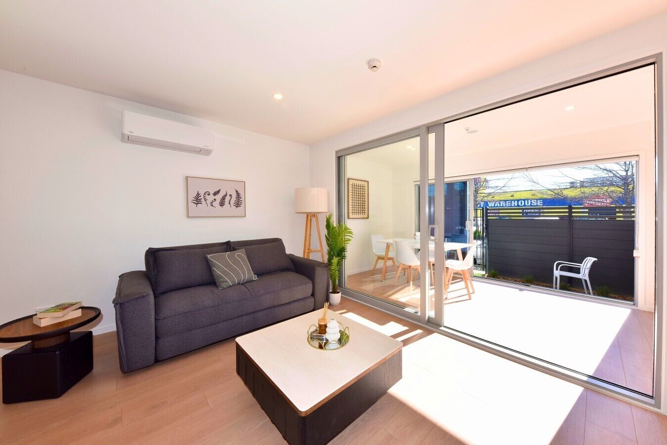 A modern living room with a grey sofa, a coffee table, and a dining area with white chairs.
