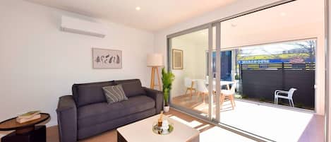 Una sala moderna con un sofá gris, una mesa de centro y un comedor con sillas blancas.