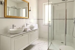 A modern bathroom with a glass shower enclosure, a large mirror, and a marble countertop.