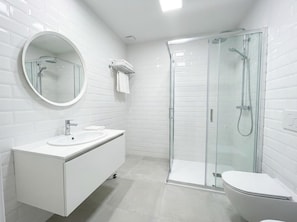 Un bagno moderno con uno specchio rotondo, un lavandino bianco, un water e una cabina doccia in vetro.