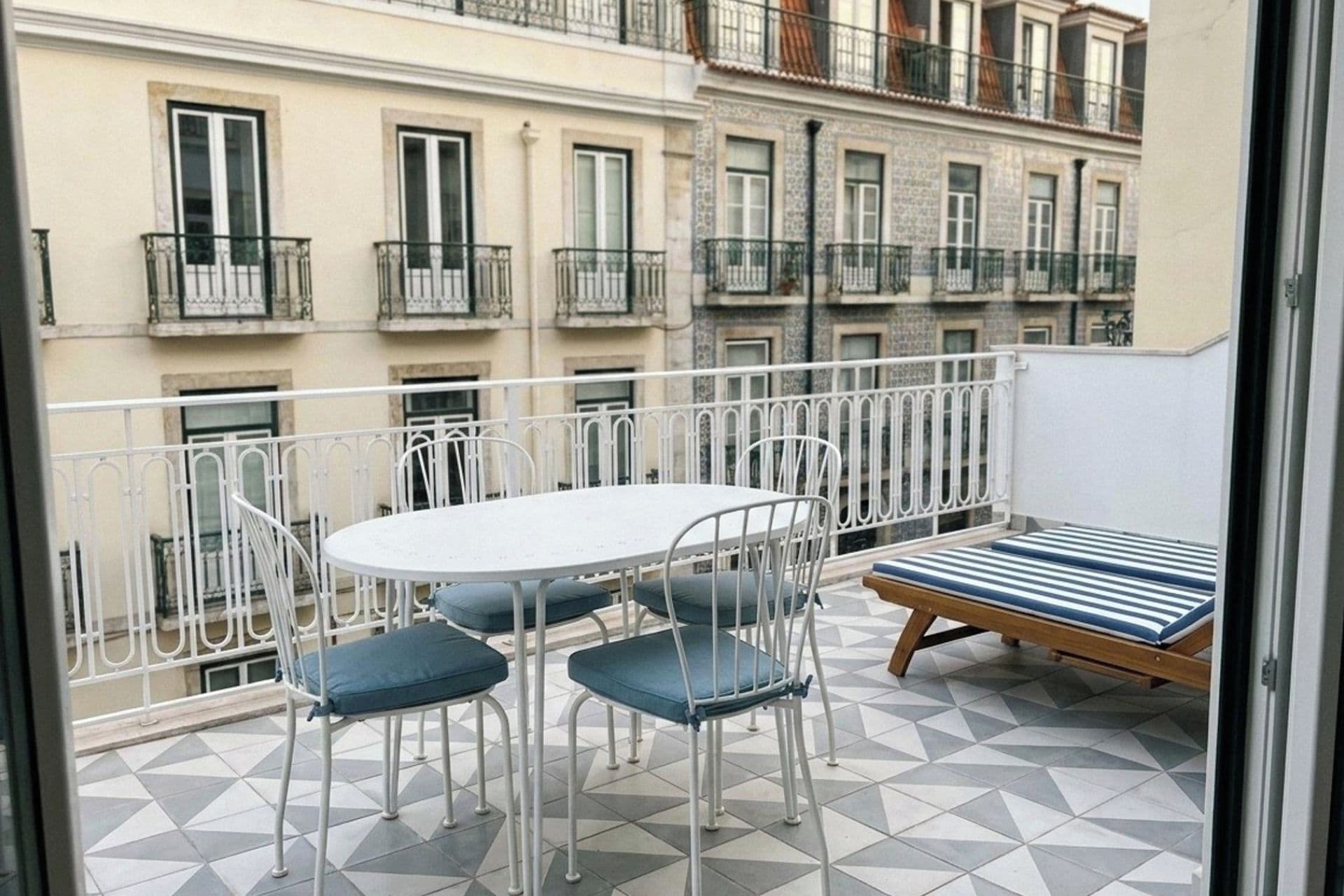 A balcony with a round table, two chairs, and a striped sofa.