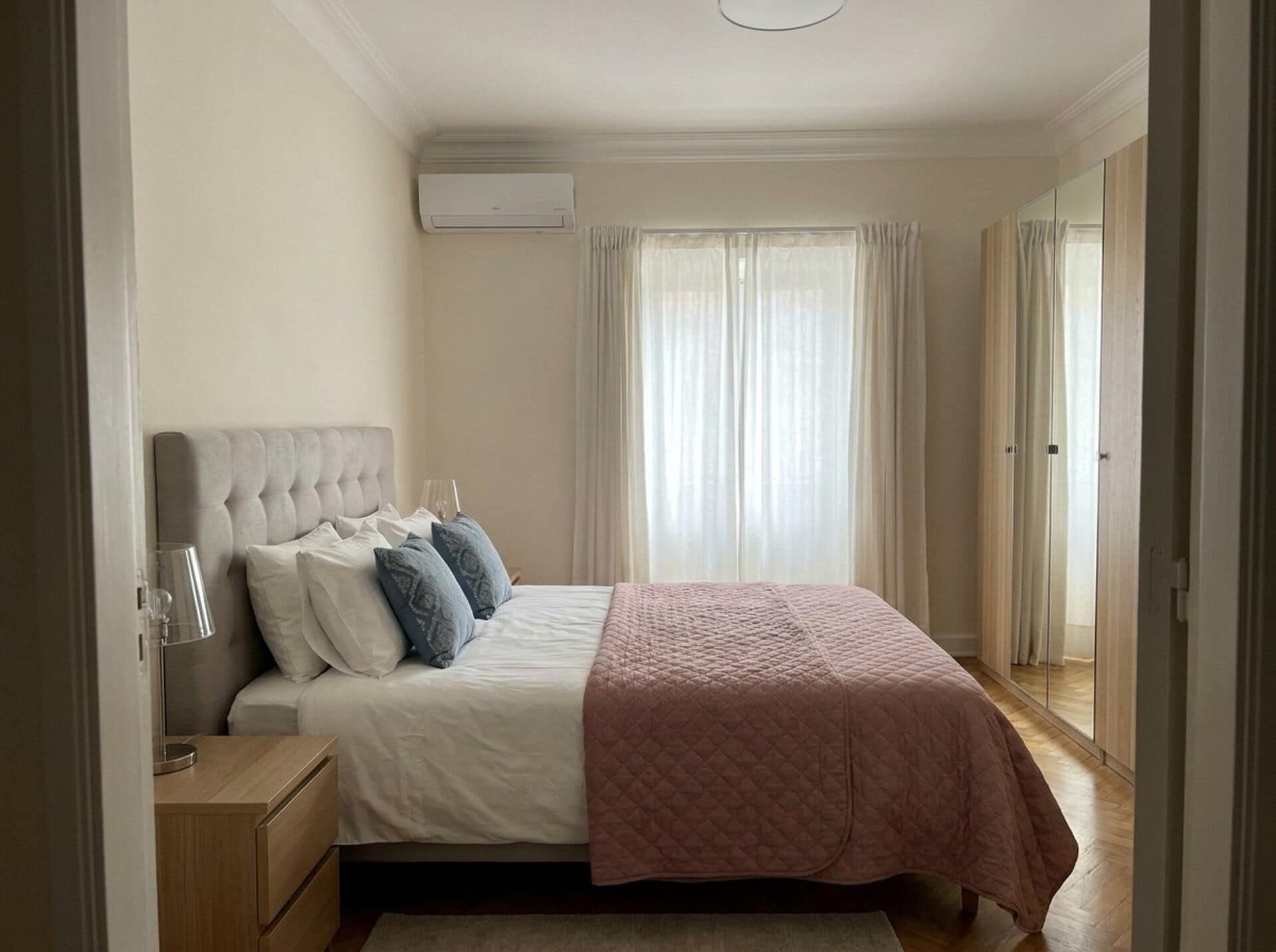 Un dormitorio con cama, mesita de noche, lámpara y ventana con cortinas.
