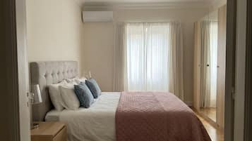 A bedroom with a bed, bedside table, lamp, and a window with curtains.