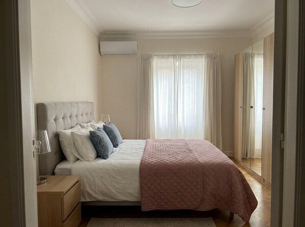 A bedroom with a bed, bedside table, lamp, and a window with curtains.