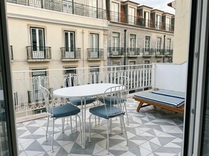 A balcony with a white table and chairs, a striped sofa, and a tiled floor. - Alfama Pearl Apartment by Ag Suites com (Lisbon)