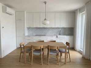 Una cucina moderna con mobili bianchi, un piano di lavoro in marmo, un tavolo da pranzo in legno con sedie e una lampada a sospensione.