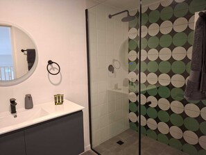 A bathroom with a glass shower enclosure, a round mirror, a white sink, and a towel rack. - Junto a la histórica Muralla del Baluarte | 1BR + 2BA | Hasta 6 huéspedes (Panamá)