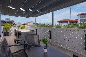 Eine Dachterrasse mit Barbereich, Sitzgelegenheiten und Pflanzkübeln.