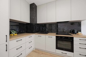A modern kitchen with white cabinets, black countertops, and a black backsplash. - Modern Apartment with Balcony | Underground Parking (Warszawa)