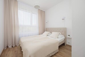 Un dormitori amb llit, cortines, una làmpada penjada a la paret i una petita planta.