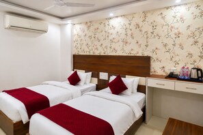 A hotel room with two beds, a wooden headboard, a floral wallpaper, a small desk with a coffee maker, and an air conditioning unit. - Hotel SGT Stay (Varanasi)