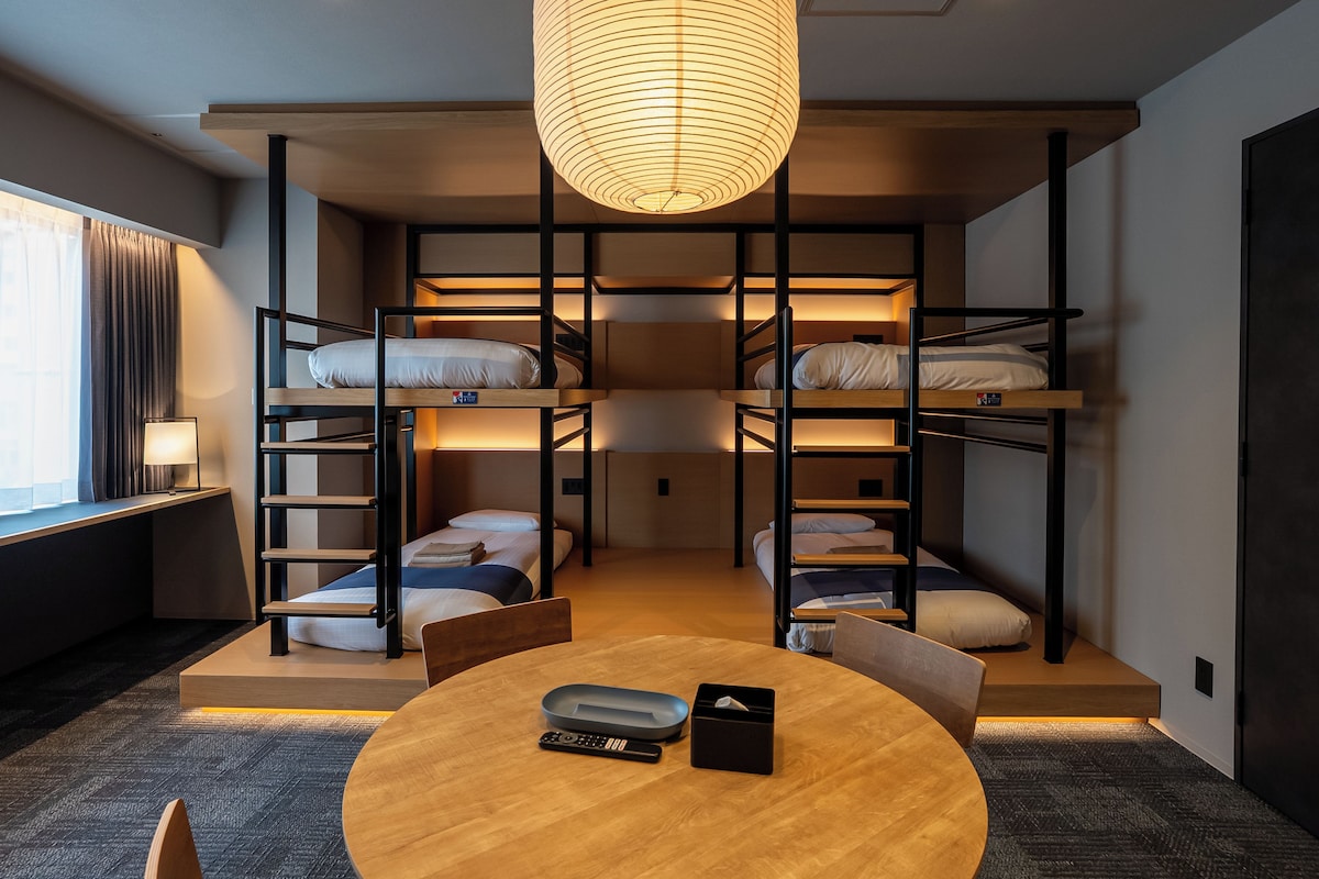 Dormitorio con literas, una mesa redonda, una lámpara y una ventana con cortinas.