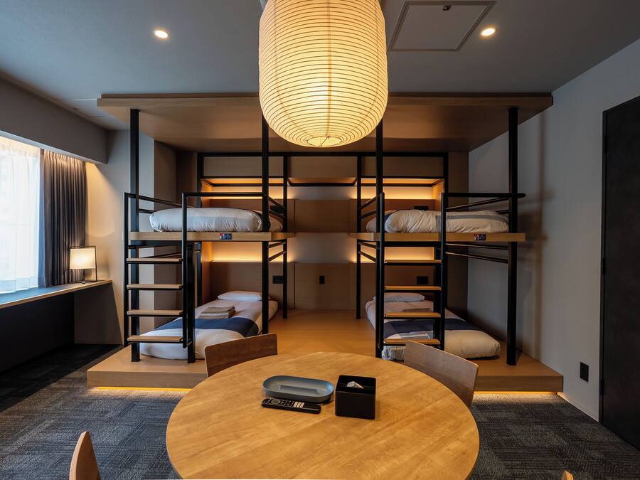 A bunk bed room with a round table, a lamp, and a window with curtains.
