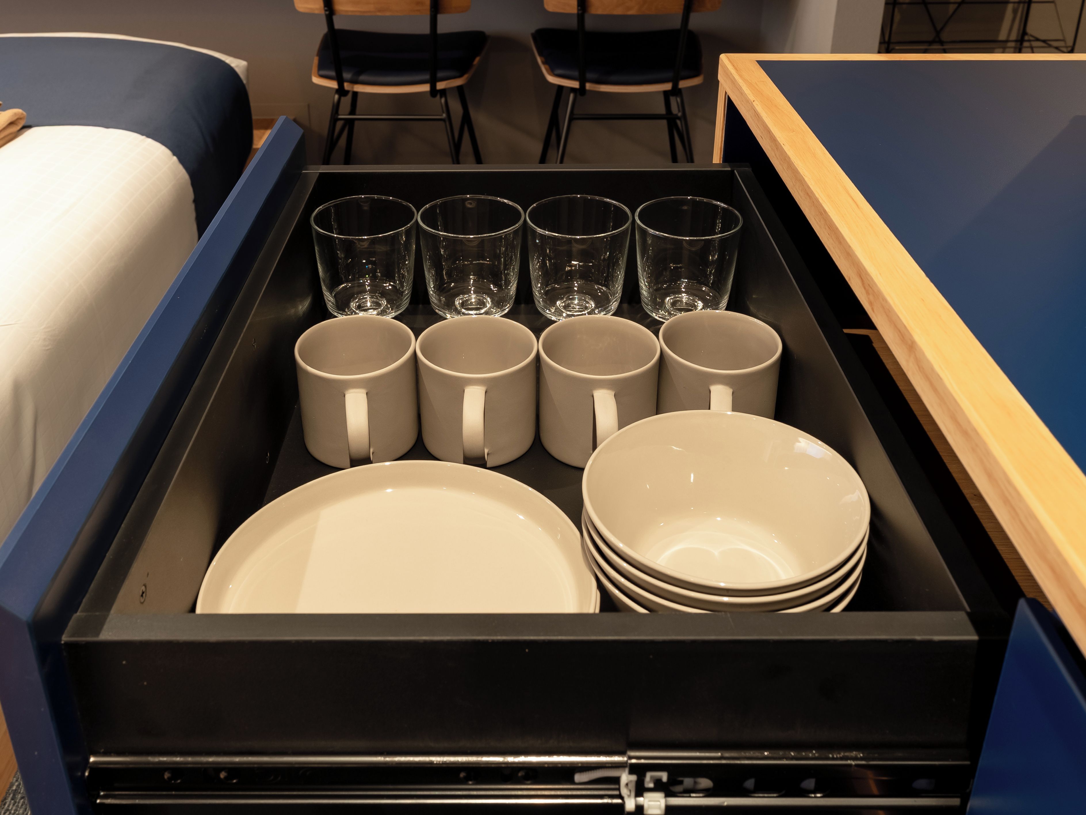 A drawer with stacked plates and mugs, and several empty glasses.