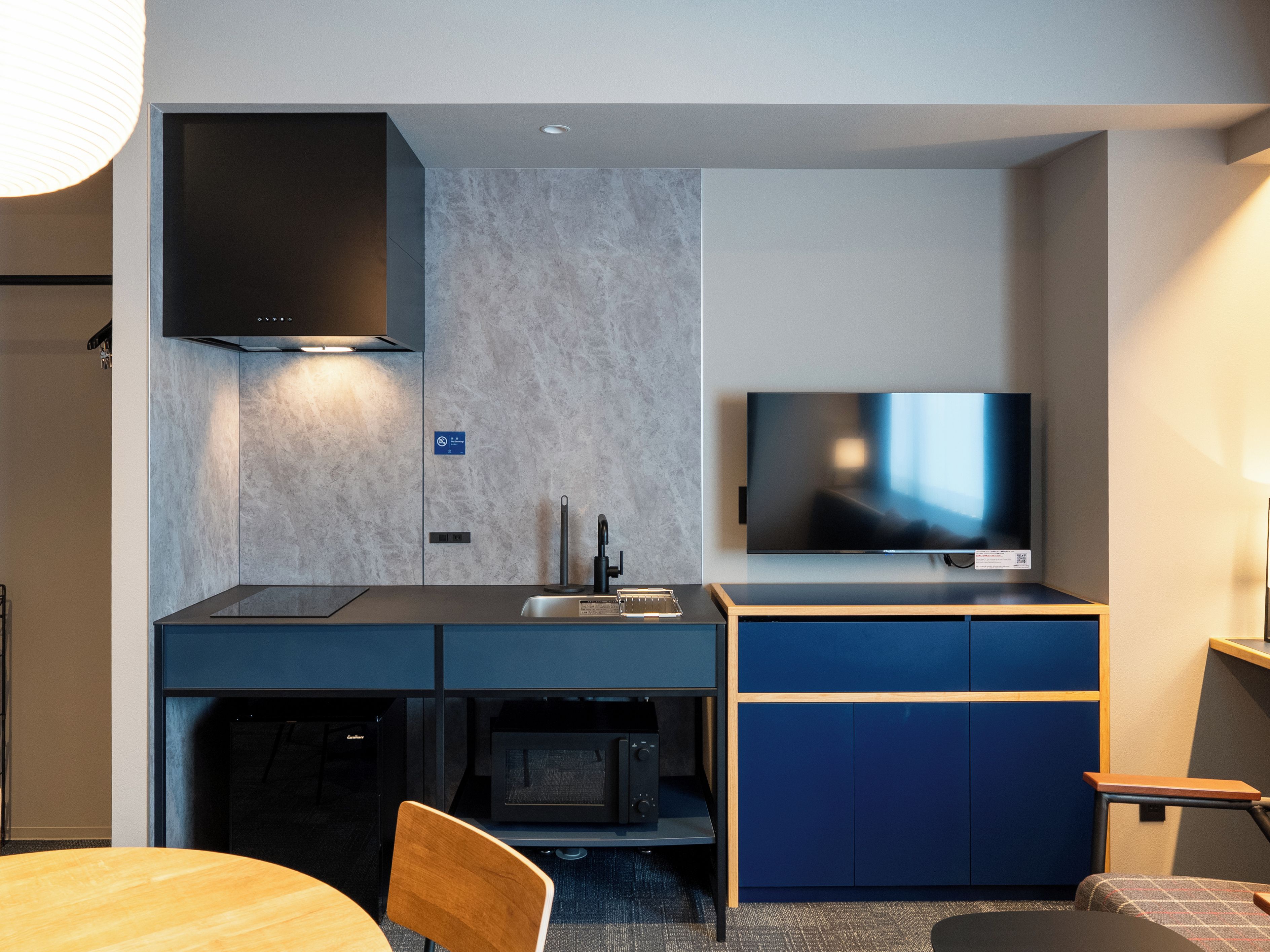 A compact kitchenette with a microwave, sink, and stove, a flat-screen TV mounted above the counter, and a dining area with a table and chairs.