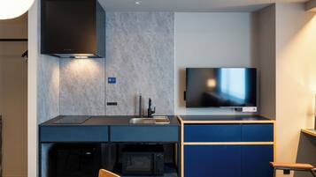A compact kitchenette with a microwave, sink, and stove, a flat-screen TV mounted above the counter, and a dining area with a table and chairs.