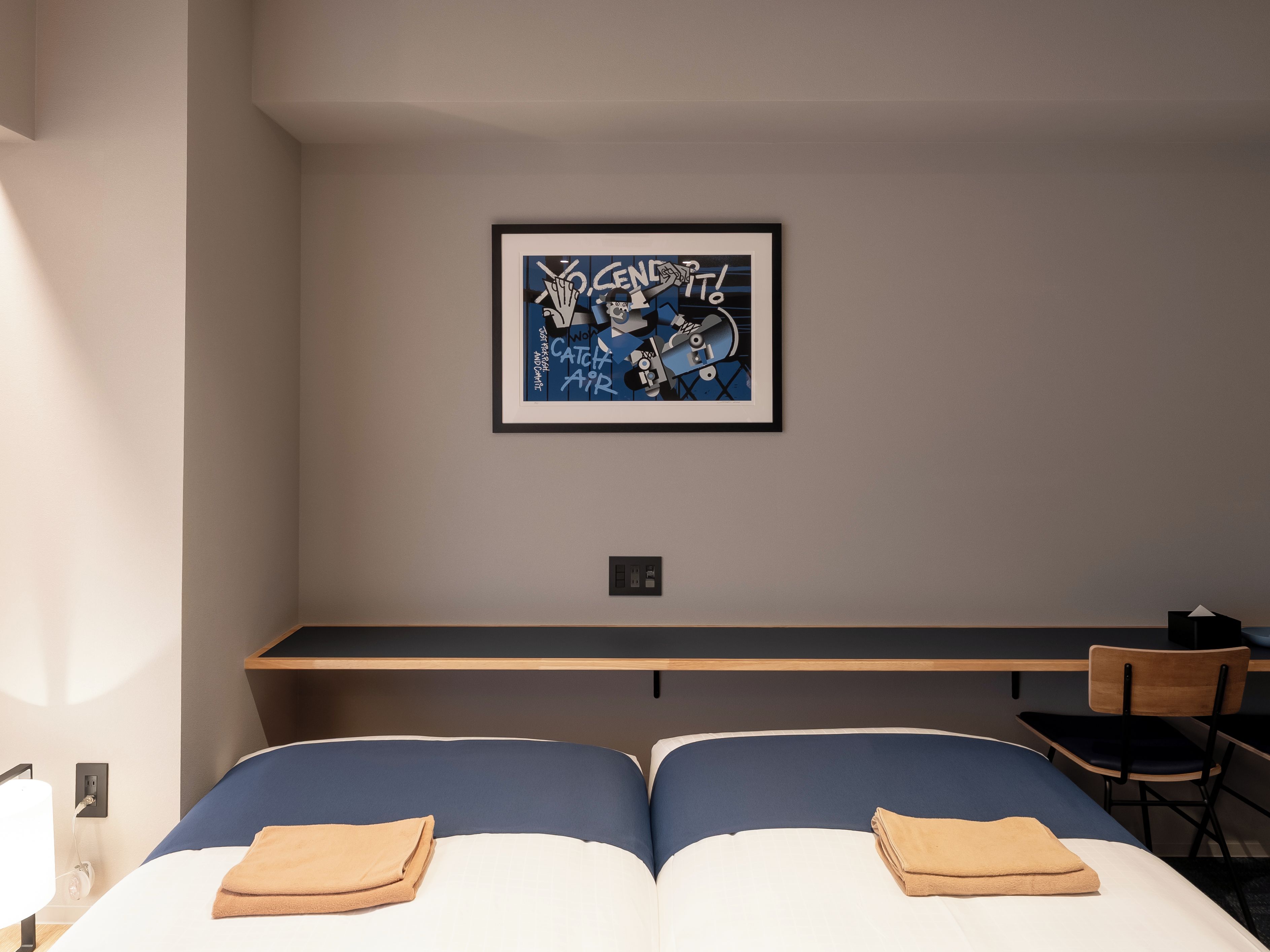 Ett hotellrum med en säng, ett skrivbord, en stol och ett inramat konstverk på väggen.