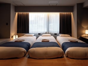 Una habitación de hotel con tres camas, un ventanal con cortinas y suelo de madera.