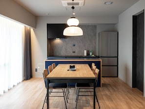 A modern kitchen with a dining area, featuring a wooden table and chairs, a pendant light, and a built-in refrigerator.
