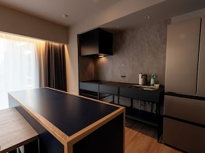 A modern kitchen with a wooden table, built-in appliances, and a window with curtains.