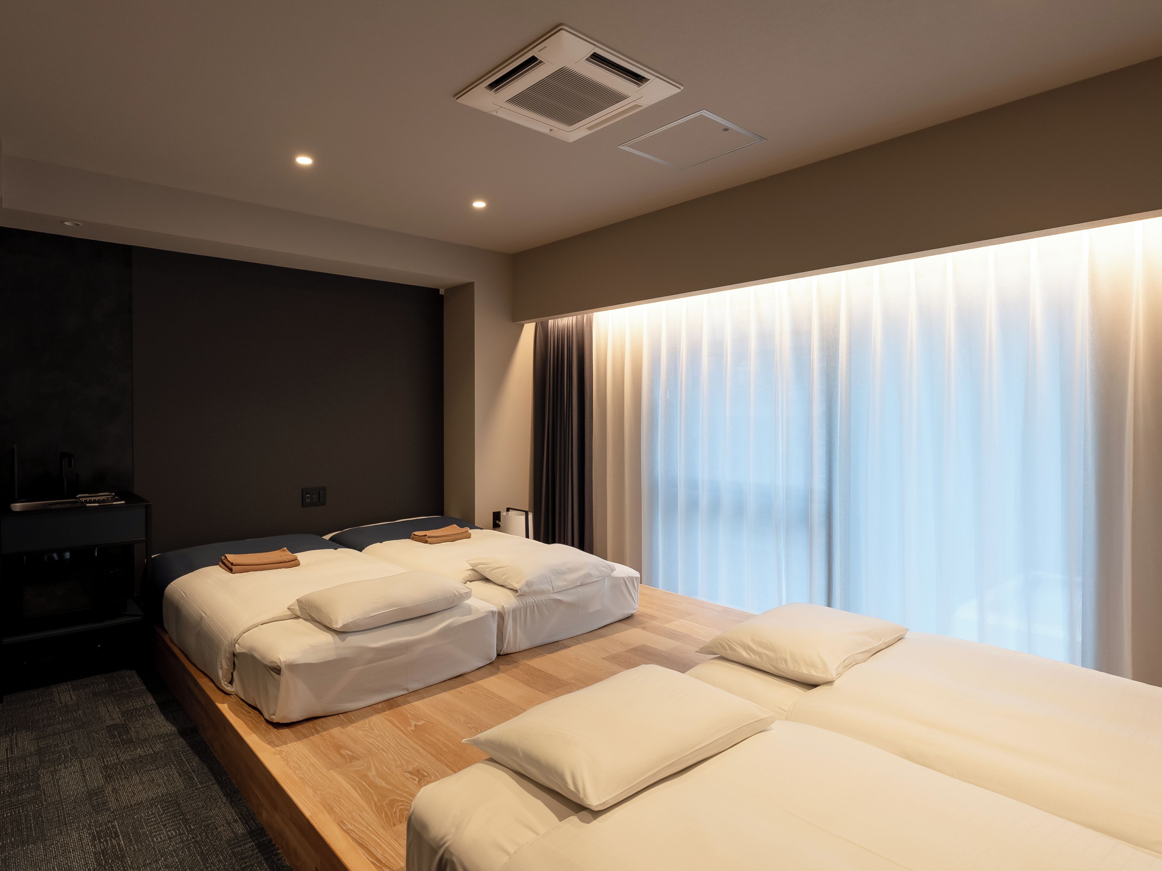 A hotel room with two beds, a desk, and a large window with curtains.