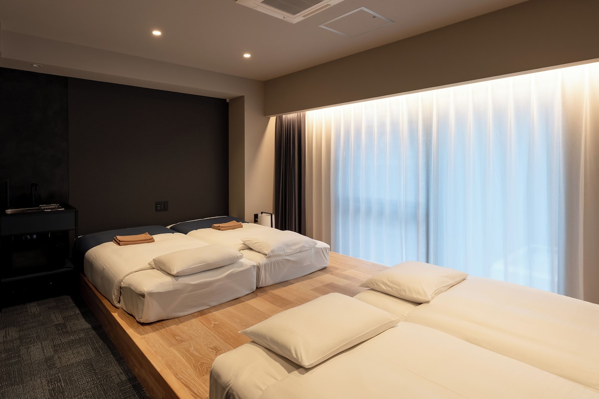 Una habitación de hotel con dos camas, un escritorio y un ventanal con cortinas.