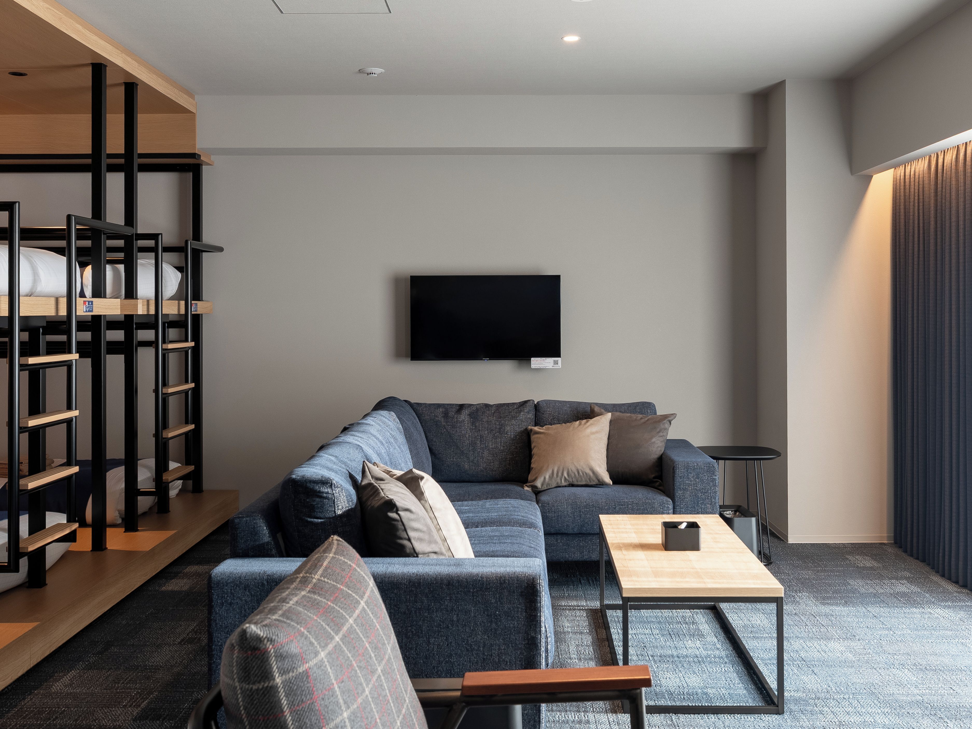 A modern living room with a sofa, a coffee table, a TV mounted on the wall, and a bunk bed structure.